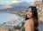 A woman looking over her shoulder smiling in front of a pretty view of a marina and the sea